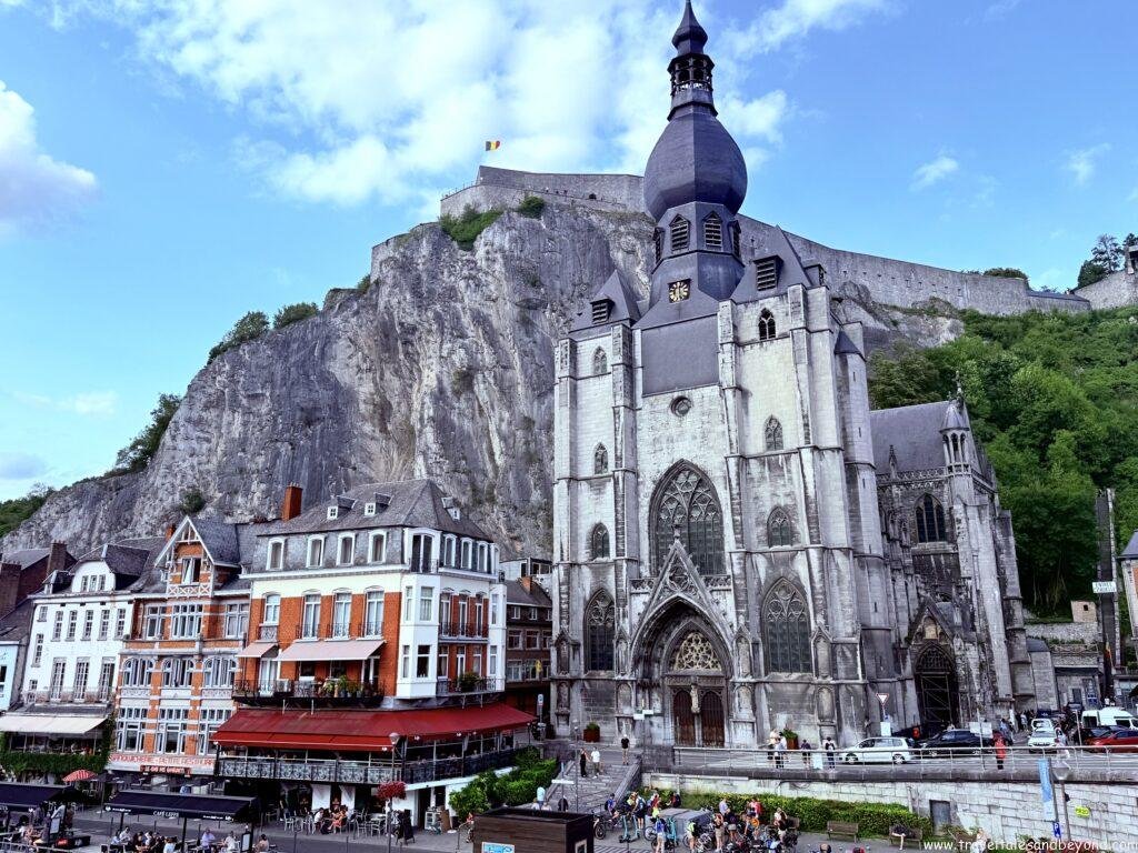 The Collegiate Church of Our Lady with its distinctive bulbous spire at the base of a sheer cliff, with the medieval Citadel visible above, Dinant, Belgium