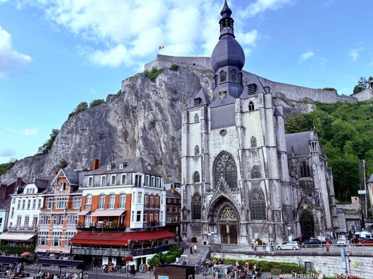 The Collegiate Church of Our Lady with its distinctive bulbous spire at the base of a sheer cliff, with the medieval Citadel visible above, Dinant, Belgium
