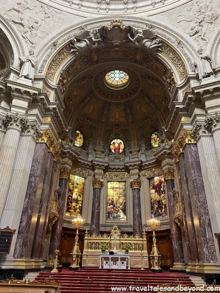 Interior of Berlin Cathedral (Berliner Dom) showing ornate Baroque altar, gold candelabras, red carpet steps, stained glass windows, and elaborately decorated dome ceiling, Berlin, Germany