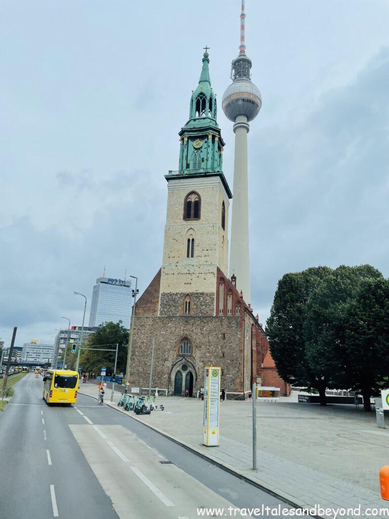 St. Mary's Church (Marienkirche) with green copper spire alongside Berlin TV Tower (Fernsehturm) at Alexanderplatz, with yellow BVG bus on Karl-Liebknecht-Straße, Berlin, Germany