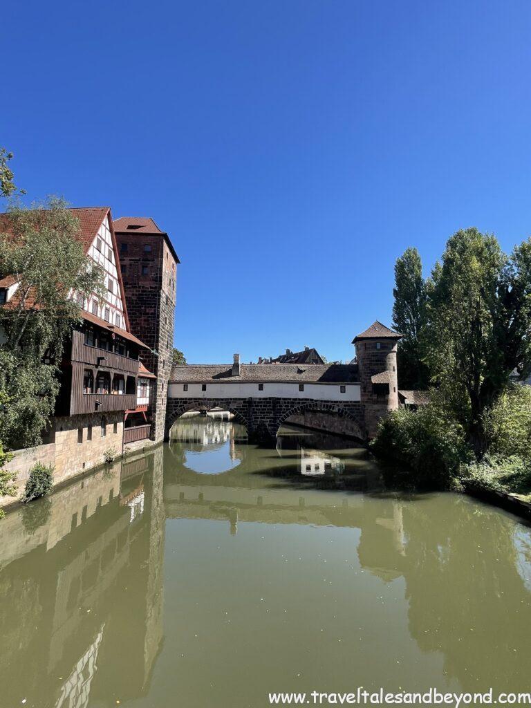 Henkersteg (Hangman's Bridge) spanning the Pegnitz River with medieval towers and half-timbered Weinstadel building reflected in calm water, Nuremberg, Bavaria, Germany