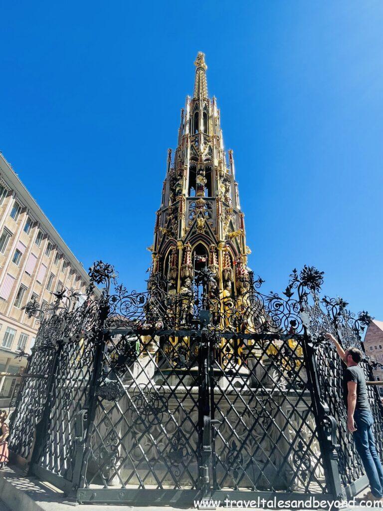 Schöner Brunnen (Beautiful Fountain), ornate 14th-century Gothic golden spire fountain surrounded by decorative wrought iron fence in Nuremberg's Hauptmarkt main square, Bavaria, Germany